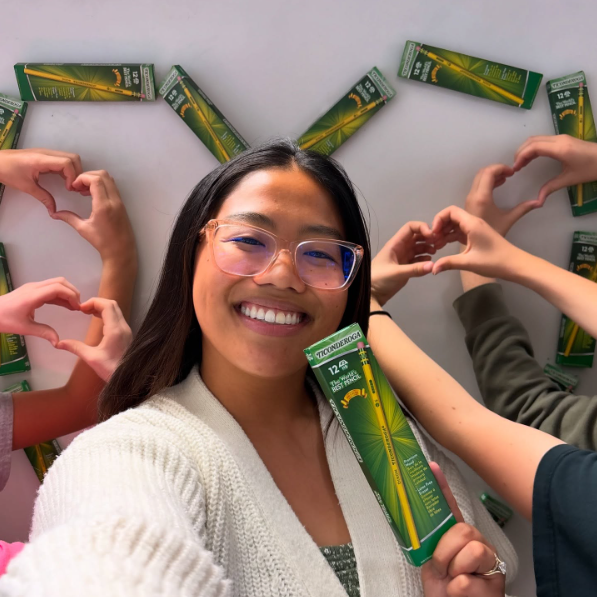 Smiling woman holds product surrounded by friends making heart shapes.