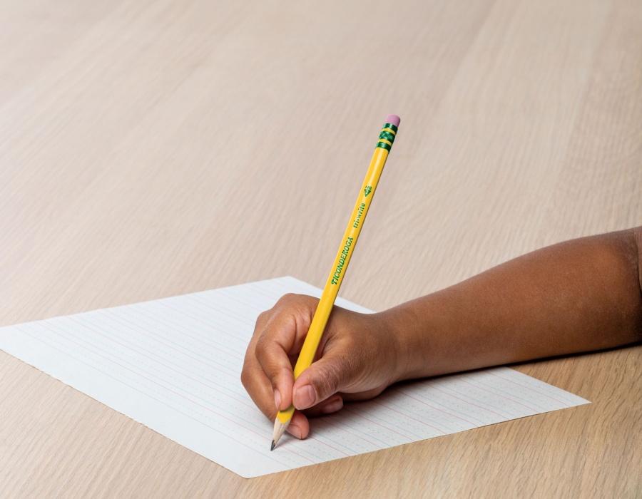 Child writing with a Ticonderoga pencil on lined paper.